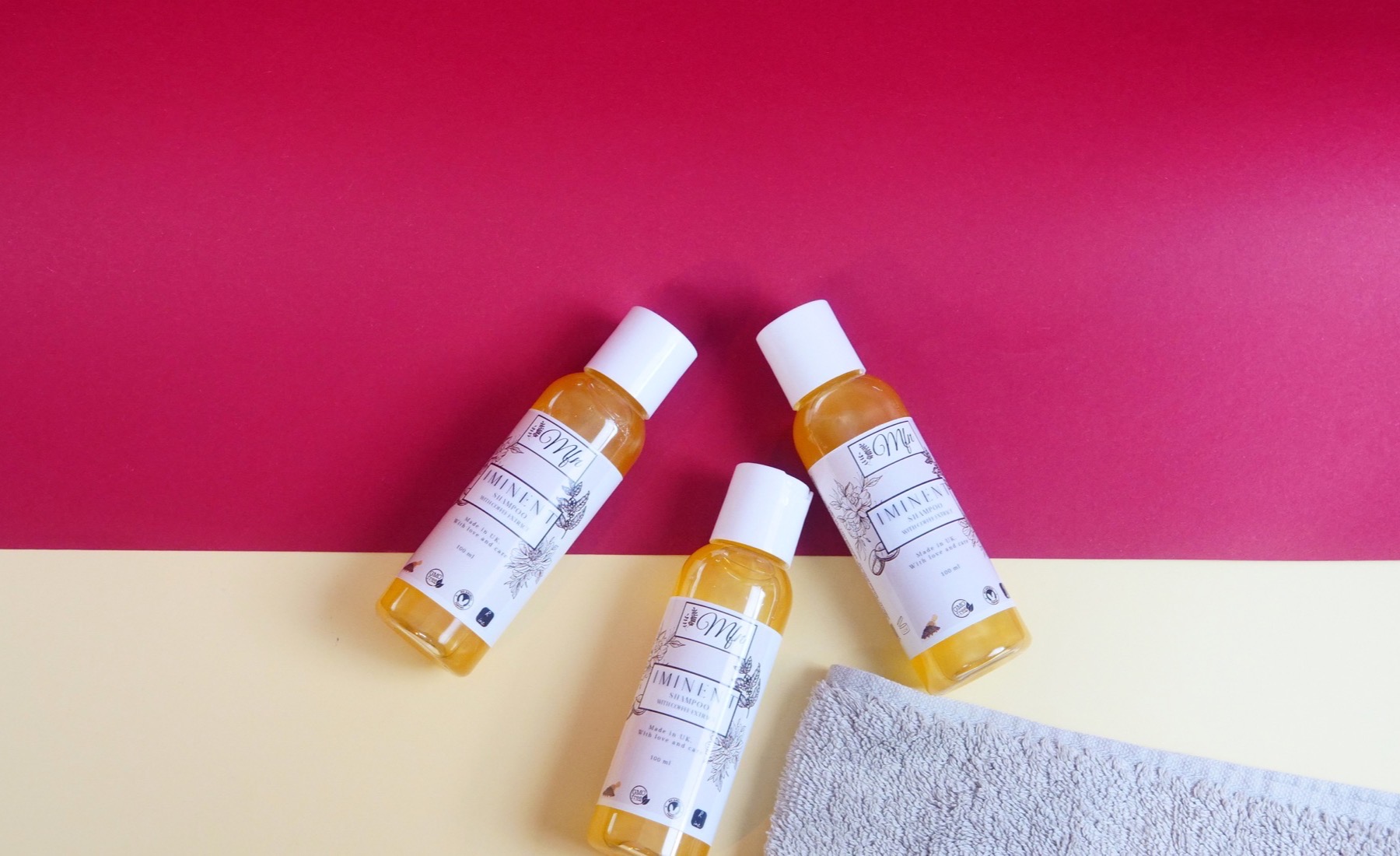 Bottles of Iminent Shampoo with caffeine extract, with a folded towel